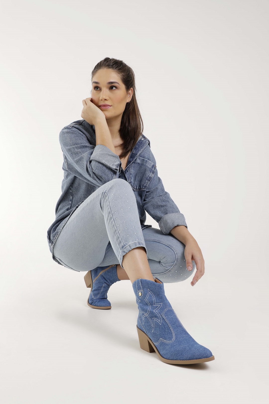 Modelo veste um look todo em jeans com camisa, calça e bota texana